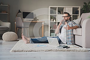 Full size profile side photo of young man sit floor home talk speak cellphone remote work laptop wear casual outfit
