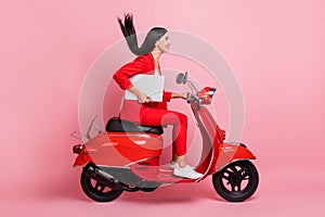 Full size profile side photo of young smiling beautiful woman riding moped with laptop isolated on pink color background