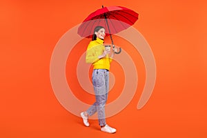 Full size profile side photo of young woman happy smile walk rain wet umbrella coffee takeaway isolated over orange