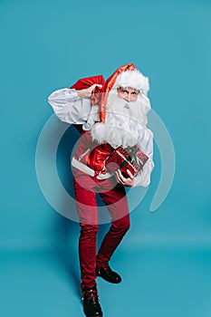 Full size of slinking santa who claus carrying huge bag of presents while holding gift box in hand