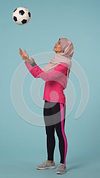 Full-sized isolated photo capturing an attractive young woman wearing a sportswear and a hijab, sheila. She is tossing