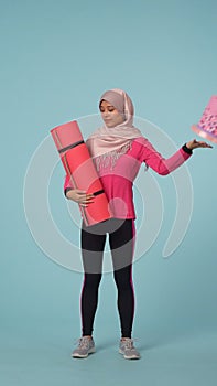 Full-sized isolated photo capturing a young woman in a sportswear and a hijab, sheila choosing between a cake and an