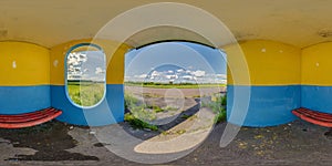 full spherical seamless hdri 360 panorama inside empty concrete bus stop painted blue and yellow with red bench inside in field