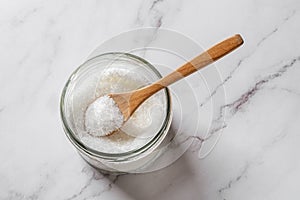 Full spoon in a jar of monosodium glutamate over kitchen marble counter. Flavor enhancer MSG white crystals in a glass container. photo
