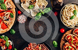 Full table of italian meals on plates Pizza, pasta, ravioli, carpaccio. caprese salad and tomato bruschetta on black background