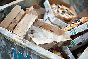 full trash bin with discarded pizza boxes and takeout containers