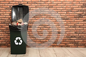 Full trash bin near brick wall indoors, space for text.