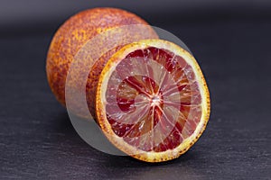 Full and two half of blood red oranges isolated on black shale background