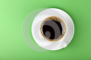 Full white cup of black coffee and saucer on green