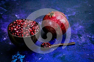 Full wooden bowl with pomegranate seeds with wooden spoon next to which there are pomegranate seeds. Whole ripe pomegranate. Bowl