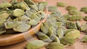 A full wooden spoon of dried green cardamom. On a textured wood surface