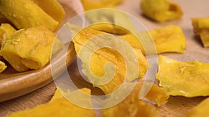 A full wooden spoon of dried sliced mango fruit. On a textured wood surface.