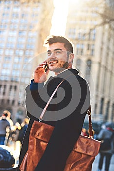 He is in full work mode today. a cheerful young man talking on his phone while waiting for a taxi to take him to work in