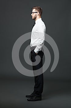 Fullbody profile view of handsome businessman on dark gray background.