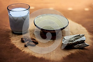 Fuller`s earth face mask in a clay bowl on brown fabric`s surface along with some milk and almonds. For softer skin