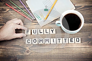 Fully committed. Wooden letters on the office desk