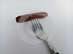 Fully cooked breakfast sausage on a fork on a white background