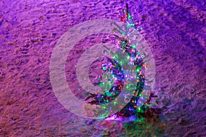 Fully decorated illuminated Christmas tree with ornaments on snowy spruce branches