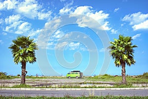 Fully equipped old timer camper van parked on the beautiful long beach between two palm trees on a bright sunny summer day