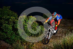 Fully Equipped Professional Downhill Cyclist Riding the Bike on the Night Rocky Trail