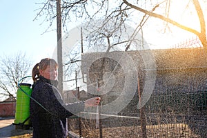 Fumigating pesti, pest control. Farmer woman spraying tree with manual pesticide sprayer against insects in spring