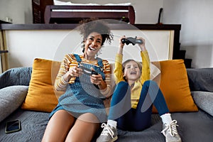 Fun. African american woman, baby sitter and caucasian cute little girl having fun together, playing video games