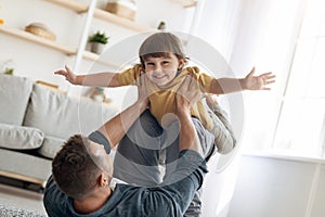 Fun with daddy. Portrait of adorable little boy playing with father at home, man lifting kid up on legs at home