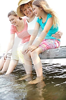 Fun on the deck. A cute young girl sitting on a pier at the lake with her mother and granny.