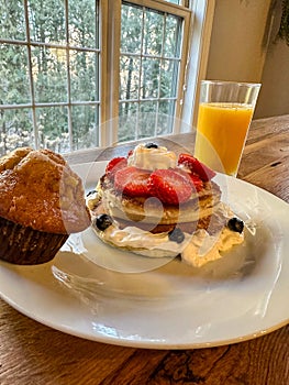 Stack of pancakes with strawberries, blueberries, bananas, and cream with juice and muffin