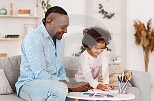 Fun family activities. Senior African American man and his curly granddaughter drawing together at home