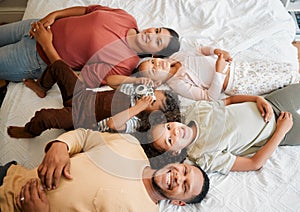 Fun family, children and parents bonding while lying on a bed in home bedroom from above. Portrait of playful, smiling