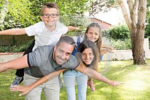 Fun family make piggyback in garden young father pretty mother glasses son and cute daughter in home park