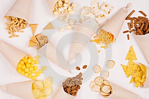 Fun fresh summer fast food background - snacks - nacho, croutons, chips, tortilla, popcorn in cone on white wood background.