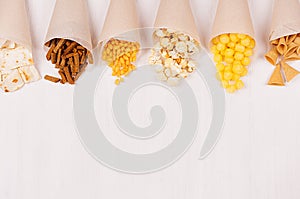 Fun fresh summer fast food background - snacks nacho, croutons, chips, tortilla, popcorn in craft paper cone on white wood board.