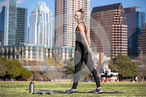 Fun friendly portrait of a beautiful and fit female athlete stretching and exercising outdoors on a sunny warm summer day in city