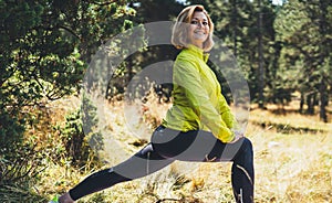Fun girl exercising outdoors in green forest, activity with stretch legs. Smile fitness woman stretching exercises training