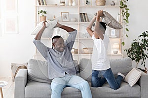 Fun With Grandpa. Cheerful Black Grandfather Pillow Fighting With Grandson At Home