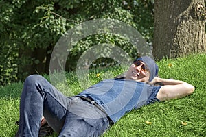 A fun guy in a bandana and sunglasses lay down on a green lawn on a sunny summer day