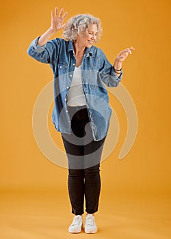 Fun, happy and cheerful woman dancing, celebrating and enjoying life alone against an orange background. Senior woman