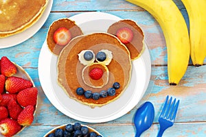 Fun idea for kids breakfast. Bear shaped pancakes with berries on blue wooden table, top view. Healthy food for children