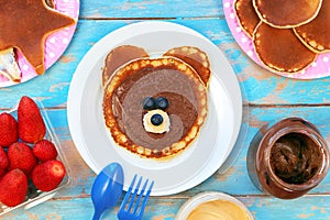 Fun idea for kids breakfast. Bear shaped pancakes with berries and chocolate paste on blue wooden table, top view