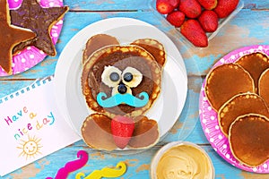 Fun idea for kids breakfast. Bear shaped pancakes with berries and chocolate paste on blue wooden table, top view