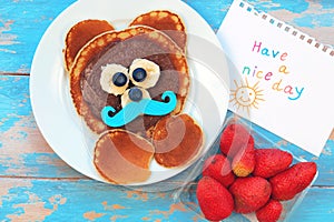 Fun idea for kids breakfast. Bear shaped pancakes with berries and chocolate paste on blue wooden table, top view