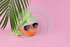 Fun idea made with an orange in sunglasses wearing a towel on his head  and palm leaf on a pink background