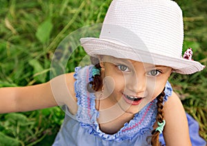 Fun kid girl in fashion hat looking excited her big eyes with humor face on summer green grass background. Closeup