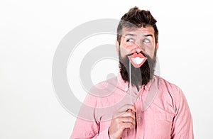 Fun and laugh concept. Man holding paper party props smiling lips, white background. Hipster with beard and mustache on