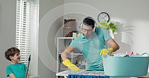 Fun in the laundry room. Dad and son doing household chores, fooling around while cleaning. Man pretends to play DJ on