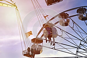 Fun in the lunapark, people on the rollercoaster and big wheel, sunset