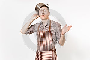 Fun man in striped apron with silver stainless glossy aluminium empty stewpan, pan or pot on head isolated on white