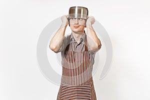 Fun man in striped apron with silver stainless glossy aluminium empty stewpan, pan or pot on head isolated on white